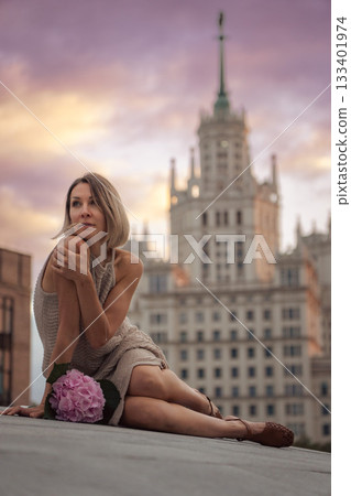 A woman sits on the Tessinsky Bridge with the Kotelnicheskaya Embankment Building rising behind her at sunset A woman sits on the Tessinsky Bridge with the Kotelnicheskaya Embankment Building rising behind her at sunset 133401974