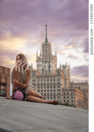 A woman sits on the Tessinsky Bridge with the Kotelnicheskaya Embankment Building rising behind her at sunset A woman sits on the Tessinsky Bridge with the Kotelnicheskaya Embankment Building rising behind her at sunset 133401984