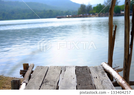 Rustic wooden bridge on riverbank with thatched building by the river for customers to dine and tropical forest background 133404257