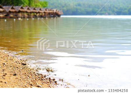 Close up sand on riverbank with thatched building by the river for customers to dine and tropical forest background Close up sand on riverbank with thatched building by the river for customers to dine and tropical forest background 133404258