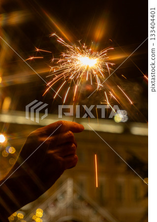 hand holding sparkler in front of Christmas tree. picture shows festive and joyful mood. 133404401