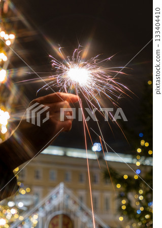 hand holding sparkler in front of Christmas tree. picture shows festive and joyful mood. hand holding sparkler in front of Christmas tree. picture shows festive and joyful mood. 133404410