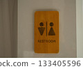 Wooden restroom sign with male and female symbols mounted on a clean white wall 133405596