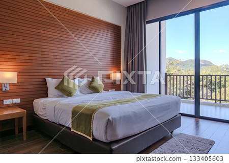 A hotel room with wooden wall paneling and soft lighting displays a large bed with white bedding and green pillows, along with bedside tables holding mounted lamps. A hotel room with wooden wall paneling and soft lighting displays a large bed with white bedding and green pillows, along with bedside tables holding mounted lamps. 133405603