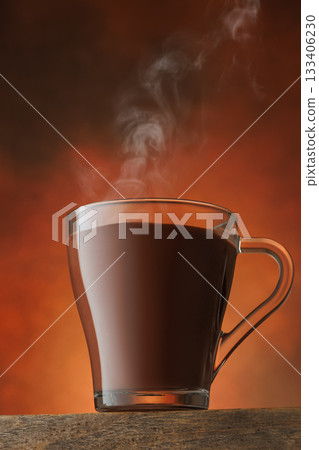 Steam rises from transparent cup of hot chocolate standing on table against brown background Steam rises from transparent cup of hot chocolate standing on table against brown background 133406230