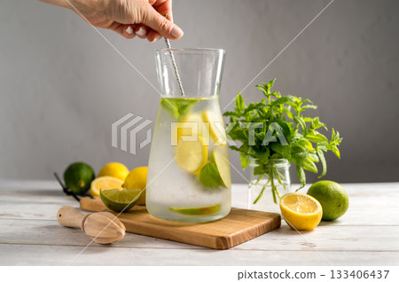 Female hand mixing lemonade with lemons, limes and fresh mint. Female hand mixing lemonade with lemons, limes and fresh mint. 133406437