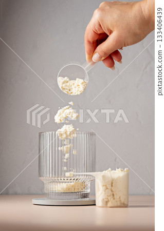 Protein powder. Pouring vanilla protein powder in a glass. Food supplement. 133406439