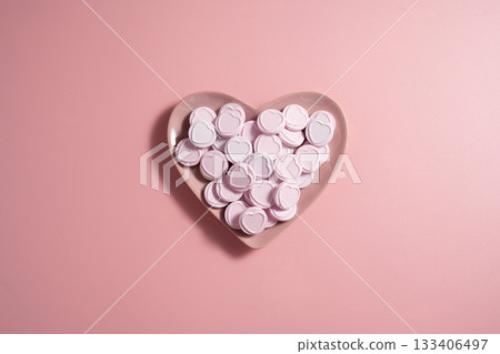 Heart-shaped candies in a pink heart plate, over pink background, abstract food love background 133406497