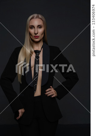 Confident model in stylish black suit with unique tie against dark background 133406974