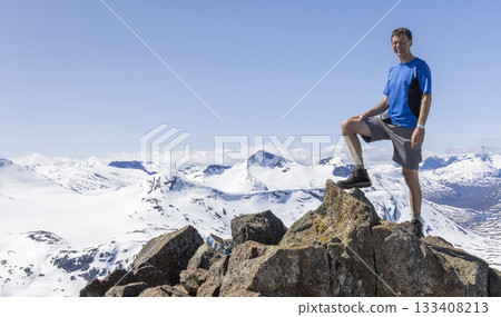 Man stands triumphantly on Kyrkja mountain overlooking snowy landscape in Jotunheimen National Park 133408213