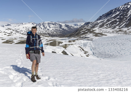 Bright winter day in snowy Leirdalen landscape near Leirvassbu in Jotunheimen National Park with a hiker enjoying the view Bright winter day in snowy Leirdalen landscape near Leirvassbu in Jotunheimen National Park with a hiker enjoying the view 133408216