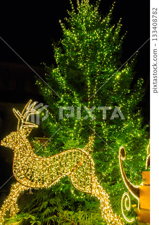 Christmas reindeer near decorated Christmas tree with multi-colored lights at night 133408782