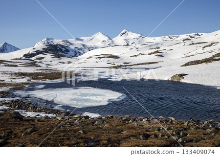 Winter landscape with melting ice and snow-capped mountains in a clear blue sky Winter landscape with melting ice and snow-capped mountains in a clear blue sky 133409074