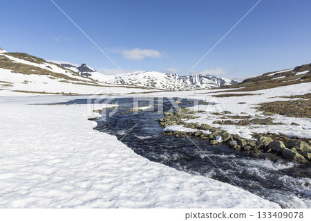 Snowy landscape of Leirvassbu in Leirdalen showcasing a flowing river in Jotunheimen National Park under a clear blue sky 133409078