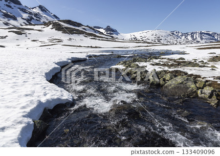 Snowy landscape with flowing stream at Leirvassbu in Jotunheimen National Park showcasing nature's beauty in winter Snowy landscape with flowing stream at Leirvassbu in Jotunheimen National Park showcasing nature's beauty in winter 133409096