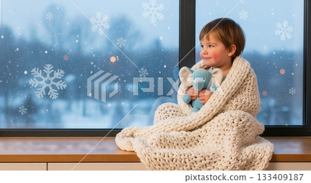 Little kid in warm blanket with toy looking at falling snow outside window. Cozy moment at home during winter for Christmas card. Little kid in warm blanket with toy looking at falling snow outside window. Cozy moment at home during winter for Christmas card. 133409187