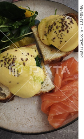 A breakfast plate with scrambled eggs, greens, tomatoes, bread and deli slices served beside a cup of coffee. Symbolizes cozy morning dining, balanced meal and a fresh start to the day 133409466