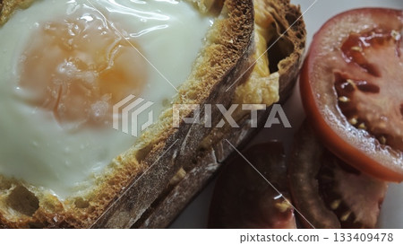 Fried egg cooked inside a slice of bread served with fresh tomato slices Fried egg cooked inside a slice of bread served with fresh tomato slices 133409478