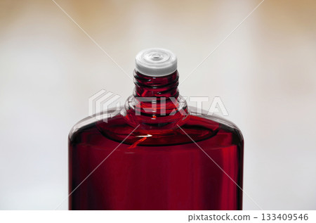 A red translucent bottle of hair growth product with the screw cap open 133409546