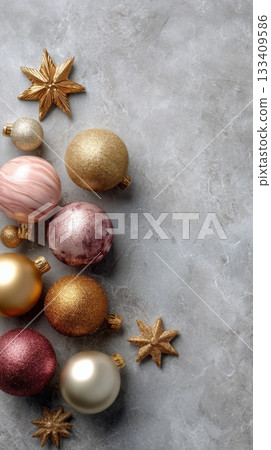 Christmas baubles and star ornaments in warm hues of gold, pink, and burgundy, arranged on a grey marble background with copy space 133409586
