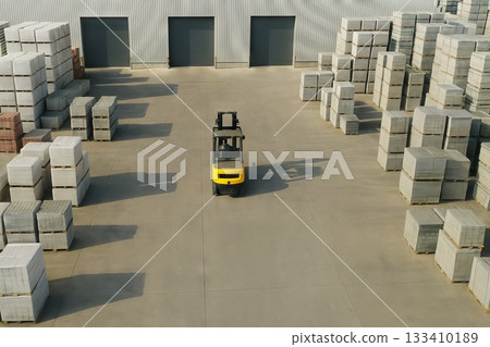 Industrial forklift moving pallet in warehouse yard surrounded by stacks of concrete blocks on a sunny day. concept of logistics, construction materials, industrial equipment 133410189