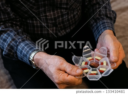 Elderly person organizing weekly medication in a pillbox at home during afternoon Elderly person organizing weekly medication in a pillbox at home during afternoon 133410481