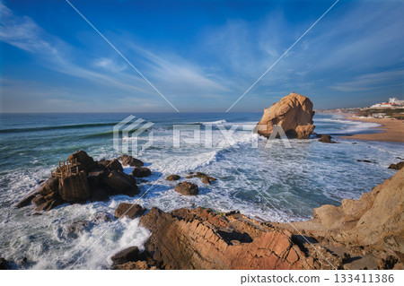 Penedo do Guincho, a large boulder rock arch at Praia da Santa Cruz, Portugal, with ocean waves and sandy beach 133411386