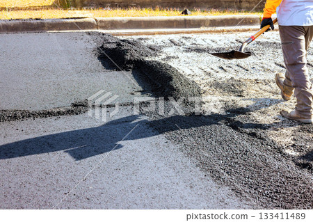 Construction worker spreads fresh asphalt on road under ensuring smooth surface. Construction worker spreads fresh asphalt on road under ensuring smooth surface. 133411489