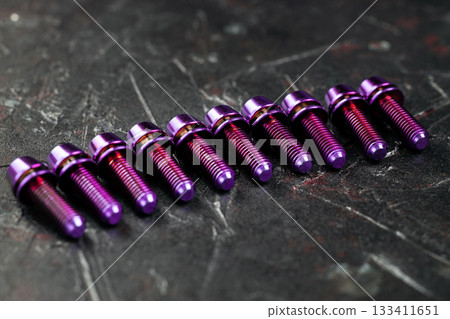 A series of titanium pink hexagon head screws on a black textured background close-up 133411651