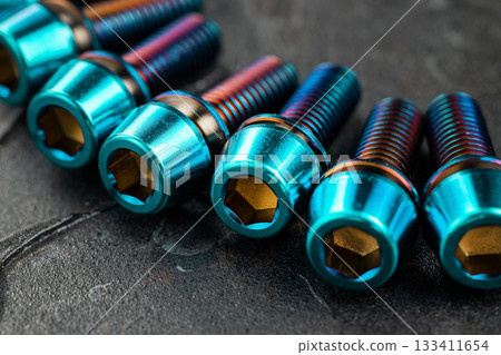 A series of titanium blue hexagon head screws on a black textured background close-up 133411654