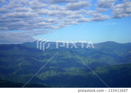 Layers of Green Rolling Hills Under a Bright Blue Sky with Scattered Clouds 133411687