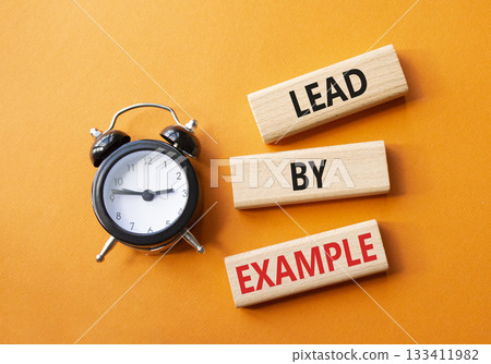 Lead by Example symbol. Concept word Lead by Example on wooden cubes. Beautiful orange background with alarm clock. Business and Lead by Example concept. Copy space. 133411982