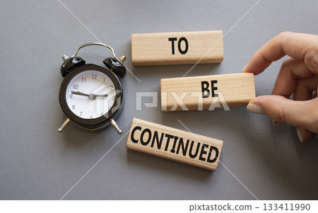 To be continued symbol. Concept words To be continued on wooden blocks. Businessman hand. Beautiful grey background with alarm clock. Business concept and To be continued. Copy space. To be continued symbol. Concept words To be continued on wooden blocks. Businessman hand. Beautiful grey background with alarm clock. Business concept and To be continued. Copy space. 133411990