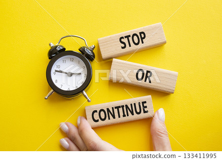 Stop or Continue symbol. Concept words Stop or Continue on wooden blocks. Businessman hand. Beautiful yellow background with alarm clock. Business concept and Stop or Continue. Copy space. 133411995