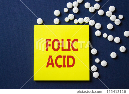 Folic acid symbol. Concept word Folic acid on yellow note. Beautiful deep blue background with pills. Medicine and Folic acid concept. Copy space Folic acid symbol. Concept word Folic acid on yellow note. Beautiful deep blue background with pills. Medicine and Folic acid concept. Copy space 133412116