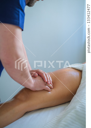 A skilled therapist performs a soothing leg and thigh massage using oil, promoting relaxation and wellness in a tranquil spa setting. 133412477
