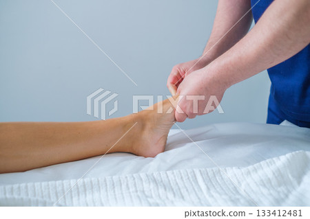 A woman enjoys a soothing foot and leg massage at a spa salon. The therapist uses oil for lymphatic drainage and relaxation. 133412481
