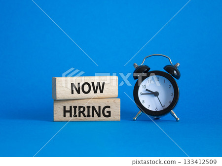 Now Hiring symbol. Wooden blocks with words Now Hiring. Beautiful blue background with alarm clock. Business and Now Hiring concept. Copy space. Now Hiring symbol. Wooden blocks with words Now Hiring. Beautiful blue background with alarm clock. Business and Now Hiring concept. Copy space. 133412509