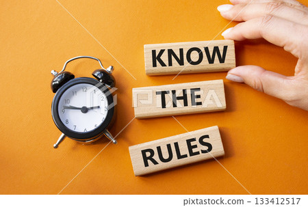 Know the rules symbol. Wooden blocks with words Know the rules. Businessman hand. Beautiful orange background with alarm clock. Business and Know the rules concept. Copy space. 133412517