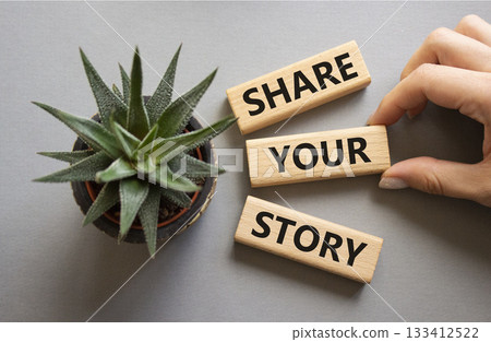 Share your story symbol. Wooden blocks with words Share your story. Beautiful grey background with succulent plant. Businessman hand. Business and Share your story concept. Copy space. 133412522