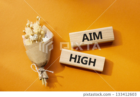 Aim High symbol. Wooden blocks with words Aim High. Beautiful orange background with bouquet of flowers. Business and Aim High concept. Copy space. 133412603