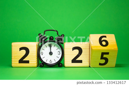 2026 New Year symbol. Businessman turns wooden cube and changes Year 2025 to 2026. Beautiful green background with Alarm clock. Copy space. Business and 2026 happy new year concept 133412617