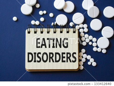 Eating Disorders symbol. Concept word Eating Disorders on notebook. Beautiful deep blue background with pills. Medicine and Eating Disorders concept. Copy space 133412640