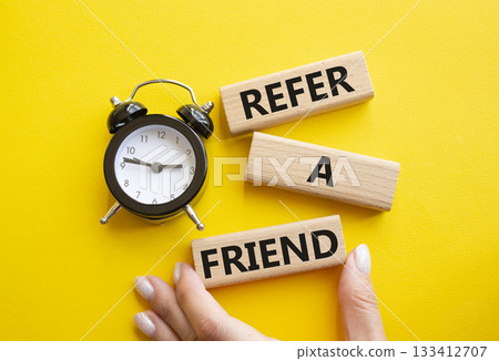 Refer a Friend symbol. Concept words Refer a Friend on wooden blocks. Businessman hand. Beautiful yellow background with alarm clock. Business and Refer a Friend concept. Copy space. 133412707