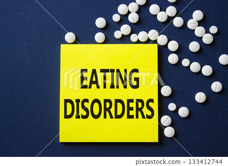 Eating Disorders symbol. Concept word Eating Disorders on yellow note. Beautiful deep blue background with pills. Medicine and Eating Disorders concept. Copy space 133412744