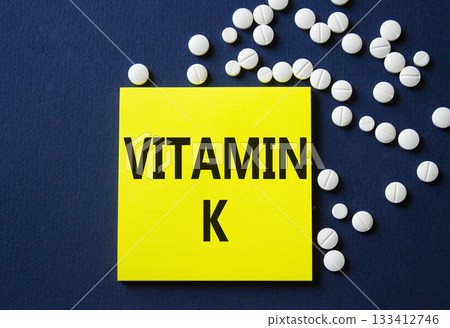 Vitamin K symbol. Concept word Vitamin K on yellow note. Beautiful deep blue background with pills. Medicine and Vitamin K concept. Copy space 133412746