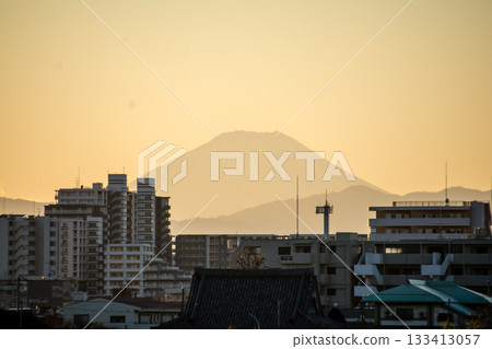 從多摩川岸邊眺望，富士山的輪廓和城市景觀在橙色的夕陽餘暉中若隱若現。 133413057