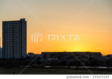 耀眼的夕陽西下，映照著寬闊的多摩川河岸，河對岸川崎的建築群清晰可見。 133413147