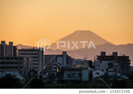 從多摩川岸邊眺望,富士山的輪廓和城市景觀在橙色的夕陽餘暉中若隱若現。 從多摩川岸邊眺望,富士山的輪廓和城市景觀在橙色的夕陽餘暉中若隱若現。 133413148