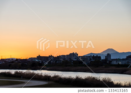 The silhouette of Mt. Fuji and the cityscape in the orange sunset sky seen from the bank of the Tama River 133413165